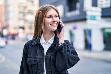 Genç sarışın kadın gülümsüyor. Kendine güveni tam. Akıllı telefondan konuşuyor.