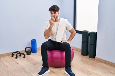 Yoga odasında pilatese oturmuş sakallı İspanyol adam ağzını eliyle kapatmaktan sıkılmış. Huzursuz ve uykulu.. 