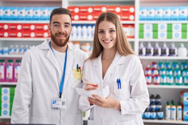Man and woman pharmacists smiling confident writing prescription at pharmacy clipart