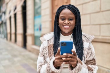 Afro-Amerikalı kadın sokakta akıllı telefon kullanarak kendine güveniyor.