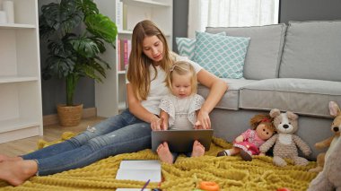 Evde, rahat bir beyaz anne ve kız dizüstü bilgisayarında bir filme dalmış, oturma odasında rahat bir şekilde oturuyorlar..