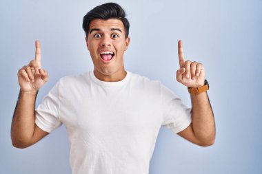Mavi arka planda duran İspanyol adam şaşırmış, şaşırmış ve parmaklarıyla işaret ediyor ve kollarını kaldırıyordu.. 