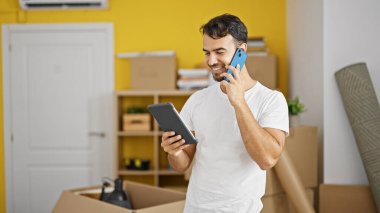 Genç İspanyol adam akıllı telefondan konuşuyor. Yeni evinde dokunmatik ped kullanıyor.