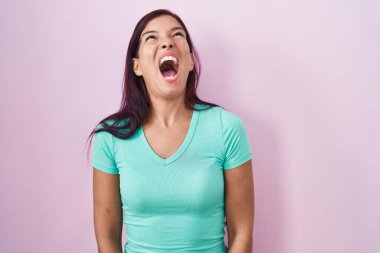 Genç İspanyol kadın pembe arka planda kızgın ve kızgın bağırıyor sinirli ve öfkeli, öfkeyle bağırıyor. öfke ve agresif konsept. 