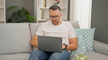 Evde dizüstü bilgisayar kullanan gri saçlı bir adam.