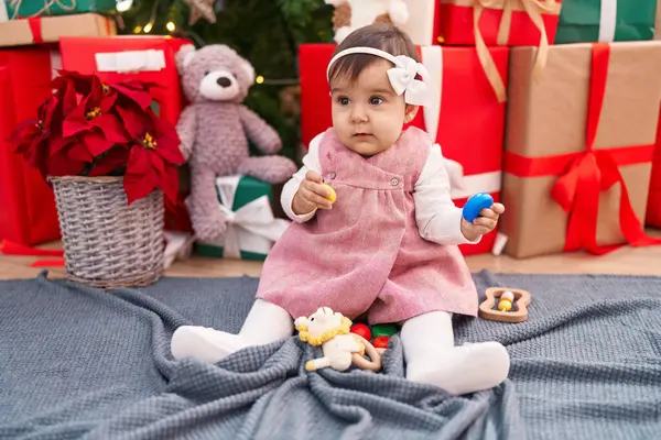 自宅でクリスマスツリーで床に座っているホップのおもちゃを保持する愛らしいヒスパニックの赤ちゃん — ストック写真