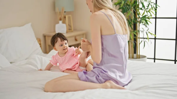 Mother and daughter sitting on bed touching feet at bedroom