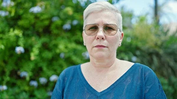 Middle age grey-haired woman standing with serious expression at park
