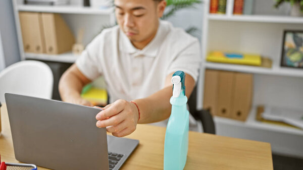 Relaxed young chinese professional man diligently working on cleaning his laptop in a calm office environment
