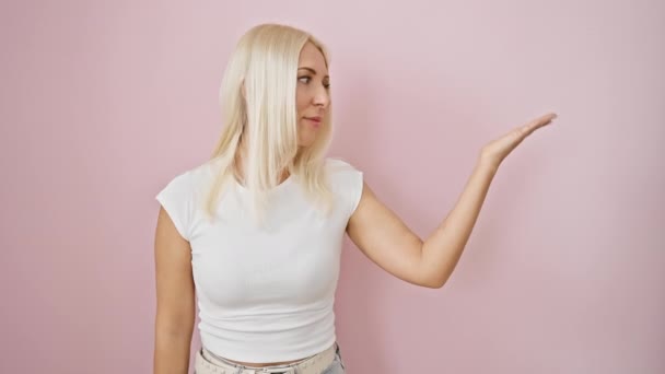 Привлекательная Блондинка Весело Указывая Представляя Ладонью Стоя Розовом Изолированном Фоне — стоковое видео