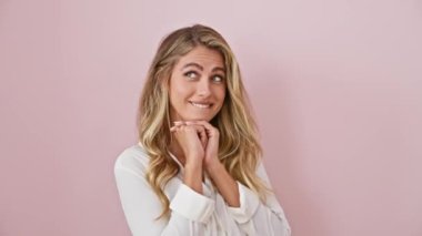 Neşeli genç sarışın kadın neşeyle gülüyor, pembe izole edilmiş arka planda duruyor, tişörtleri üstünde, elleri çenesinde neşeli ifadesini gösteriyor.!