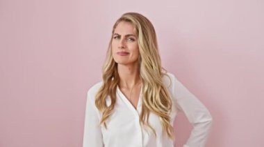 Kendine güvenen genç sarışın kadın klasik İtalyan el hareketleriyle poz veriyor. Pembe arka planda duruyor. Sıradan bir gömlek giyiyor.