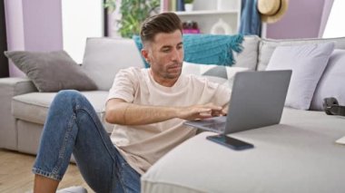 Çekici İspanyol asıllı genç adam oturma odasında yoga egzersizleri yaparak dengeyi buluyor, evde internet üzerinden rahatlama ve meditasyon yaparak, sağlık yaşam tarzını kucaklayarak.