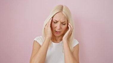 Şiddetli migren ağrısı çeken stresli sarışın kadın, soyutlanmış pembe arka planda tek başına duruyor, elini başını tutuyor..