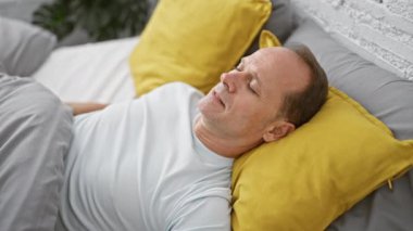 Orta yaşlı bir adam yatakta uzanıyor, yatak odasında uyuyor.