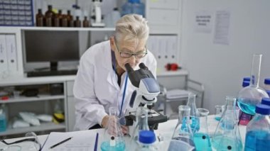 Kendine güvenen, gülümseyen, gri saçlı, işinde mutlu, laboratuvarda mikroskobu ustaca kullanan tıp araştırma merkezindeki olgun bilgeliğine bilim adamı..