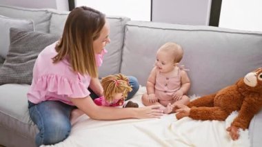 Mutlu anne akıllı telefondan konuşuyor, sevimli kız kanepenin üzerinde oyuncak bebeklerle oynuyor, evde birlikteliğimizi ifade ediyor.