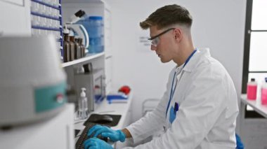 Çekici, beyaz erkek bilim adamı test tüpleri ve mikroskoplar arasında bilgisayara kendini tamamen kaptırmış durumda.