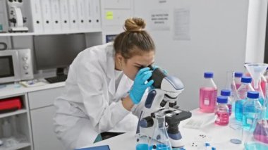 Bilim adamı üniforması içindeki neşeli İspanyol kadın, kollarını açıp kameraya sarılıyor ve gülümsüyor. Laboratuvarda mutluluk saçıyor.