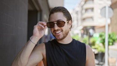 Sokakta güneş gözlüğünü çıkarırken gülümseyen İspanyol genç adam.