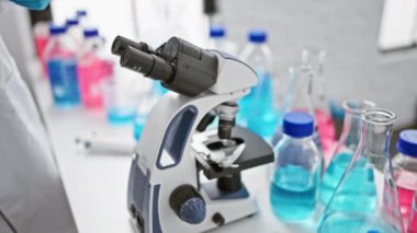 Güzel saç stili olan kararlı genç İspanyol bilim kadını laboratuvarda mikroskop teknolojisi kullanarak ciddi araştırmalara daldı..