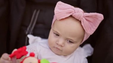 Sevimli, ciddi yüzlü bebek bebek bebek bebek koltuğunda rahatlıyor. Kurdeleyle sarılmış küçük bir vücutta rahatlık. Giysiler içinde şirin.