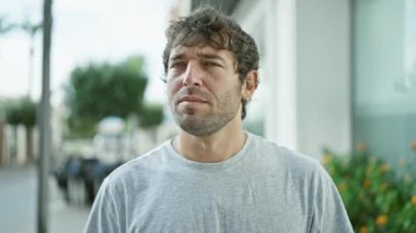 Sakallı, sarı saçlı, kendine güveni tam bir genç adam, ciddi bir ifadeyi tasvir ediyor ve bir şehir caddesinde dururken kendine güvenen bir 