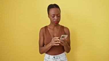 Neşeli Afro-Amerikan kadın, akıllı ve kendinden emin, parlak bir fikirle bir parmağını yukarı kaldırıyor, güneşli sarı izole bir arka planda akıllı telefonuna gülümsüyor.