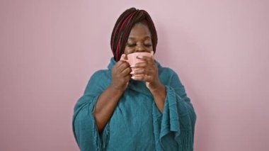 Örgü örmüş neşeli Afro-Amerikalı kadın, sabah kahvesinin tadını çıkarıyor, pembe arka planda tek başına duruyor.