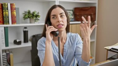 Genç, güzel, İspanyol bir iş kadını ofiste telefonla konuşuyor.