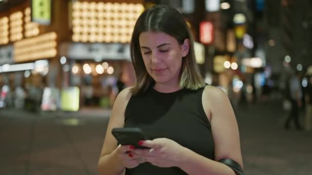 美丽的惊慌失措的女人在东京的城市夜灯前微笑着 一边用智能手机愉快地发短信 — 图库视频影像