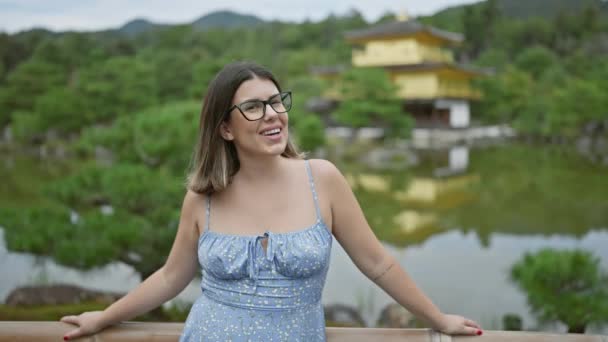 魅力的なヒスパニック女性は 彼女が笑顔で輝く喜び 息をのむようなキンカク寺の金のパビリオン 京都の宝石で彼女の眼鏡に自信とカジュアルを立っています — ストック動画