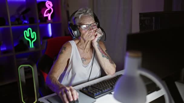 灰色の髪の女性ストリーマーがゲームの夜を支配し 高齢女性は薄暗く明るいホームオフィスからゲームの世界をロックします — ストック動画