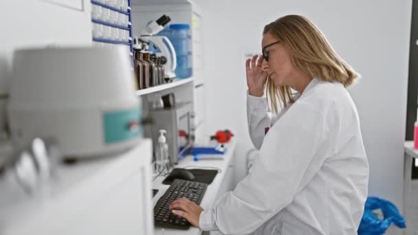 在生物研究实验室紧张的计算机工作中 身穿实验室外套 专注于研究的年轻科学家们摘下了她的眼镜 — 图库视频影像