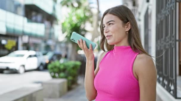 若いヒスパニック系女性を笑顔でアウトドアを楽しませ スマートフォンで活発な音声メッセージを送る — ストック動画