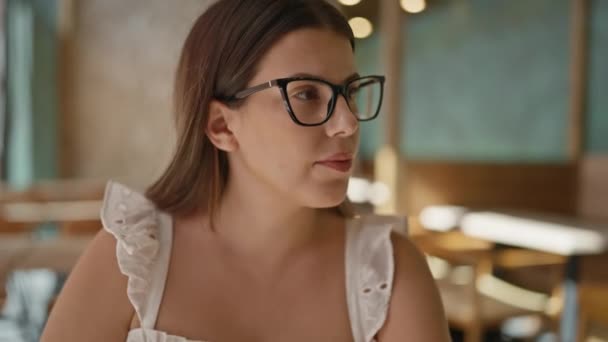 美しい若いヒスパニック系女性は カフェテリアでグラスを飲みながらメガネをかけている — ストック動画