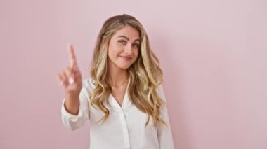 Tişörtlü neşeli sarışın güzel, bir numaralı parmağıyla, kendinden emin bir şekilde, canlı pembe bir arka plana gülümsüyor.