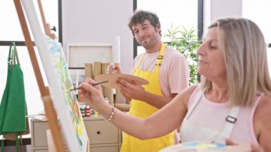 İki kendine güvenen sanatçı, erkek ve kadın, gülümsüyor, oynuyor ve resim stüdyosunda birlikte resim çiziyorlar.