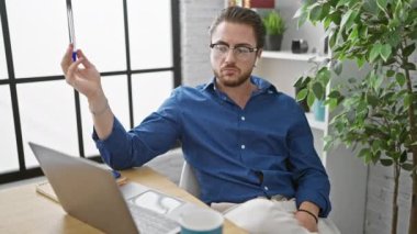 Genç İspanyol iş adamı, ofiste dizüstü bilgisayar ve kulaklık kullanıyor.