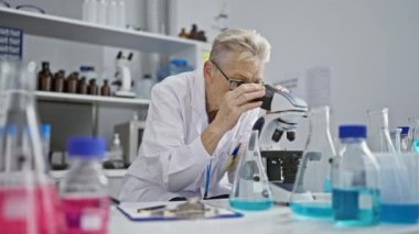 Bilimin kalbinde, ciddi bir gri saçlı kıdemli kadın bilim adamı, laboratuvarında sıkı çalışıyor, mikroskopla son bulgularını incelerken titizlikle not alıyor..