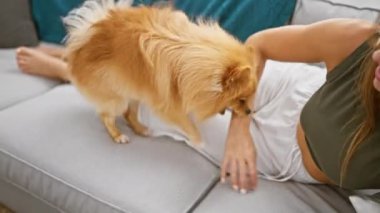 Evdeki rahat oturma odasında, sevimli köpeğiyle şakalaşan, kanepede uzanan, mutluluk saçan ve sevgi dolu bir İspanyol kadının içten içe portresi..