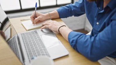 Genç İspanyol iş adamı laptopunu ofiste not alıyor.