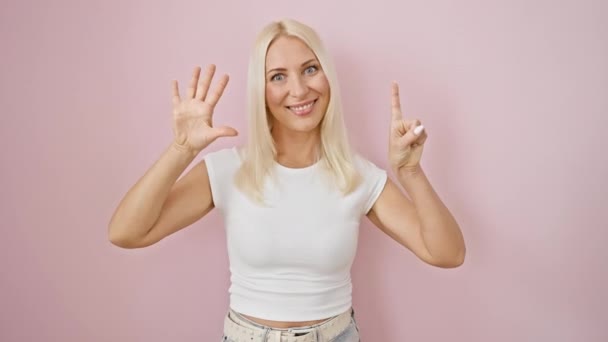 年轻快乐的金发女子带着自信而快乐的微笑 用手指展示了第六位 站在粉红色孤立的背景之上 — 图库视频影像