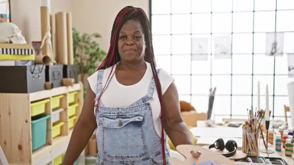 アフリカ系アメリカ人女性アーティストの笑顔が活気あふれるアートスタジオで自信を持ってペイントブラシとパレットを振り回す — ストック動画