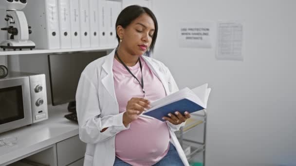 怀孕的年轻女科学家沉浸在实验室工作站所读到的一本深奥的化学书籍中 将母性和医学研究融为一体 — 图库视频影像