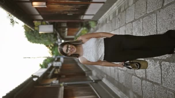 他那快乐的惊慌失措的女人高兴地摆姿势 眼镜闪闪发光 站在传统的京都街道中间 被日本建筑迷住了 她那美丽的微笑散发着自信 — 图库视频影像