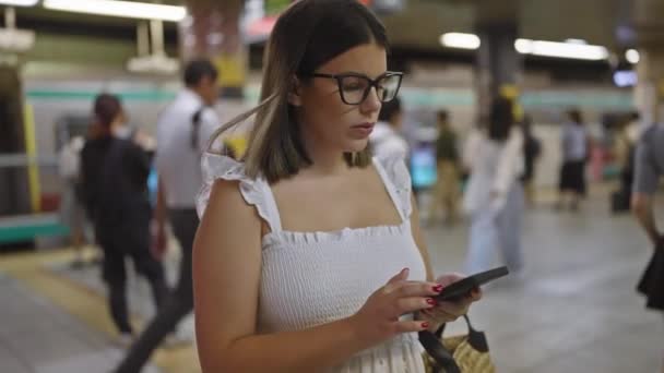 他惊慌失措的女人 戴着眼镜 站在地铁站前 等待着她的地铁之旅 全神贯注地听着她的电话 — 图库视频影像