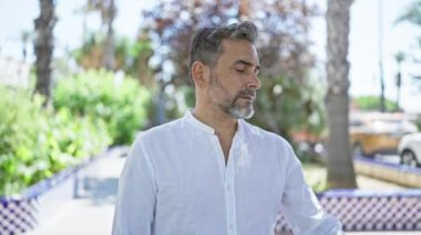 Sakallı, kır saçlı, yeşil parkta gülümseyen ve dışarıda duran kendine güvenen genç İspanyol adam gökyüzüne ve kol saatine bakarken geç kalabileceğinden endişe ediyordu.