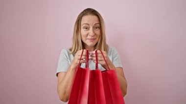 Neşeli genç sarışın kadın, şık bir alışveriş meraklısı, moda alışveriş torbalarına mutlu bir şekilde bakıyor, perakende terapi skoruna şaşırmış, pembe bir arka planda izole edilmiş..