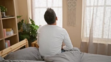 Yakışıklı, beyaz saçlı, kollarını uzatan genç bir adam, rahat bir yatakta uyanıyor, rahatça dinlendirici bir yatak odası düzeninde.